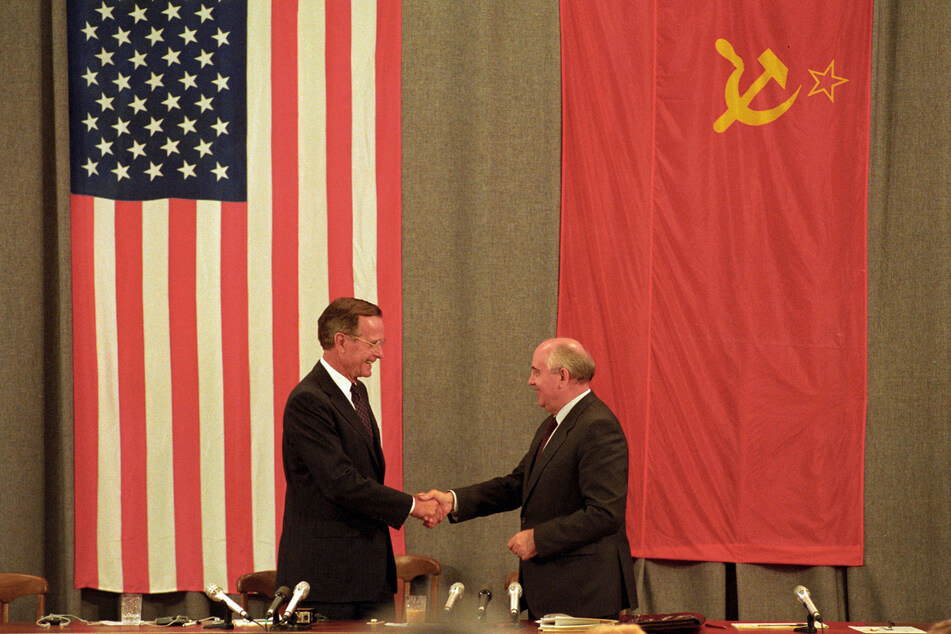 US President George H. W. Bush (l.) and Soviet President Mikhail Gorbachev shake hands in front of US and Soviet flags at the end of a press conference in Moscow on July 31, 1991.