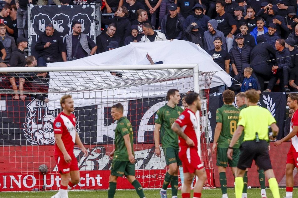 Die werfenden Fans haben sich unter einem weißen Banner versteckt.