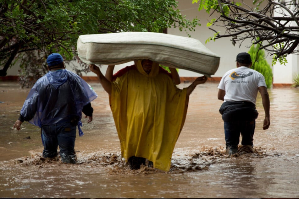 Guatemala, Agua Blanca: Zwei Männer tragen eine Matratze durch eine überschwemmte Straße.