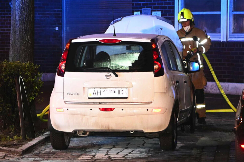 Ein Feuerwehrmann löscht vor der Justizvollzugsanstalt Berlin-Moabit ein Auto mit ukrainischem Kennzeichen.