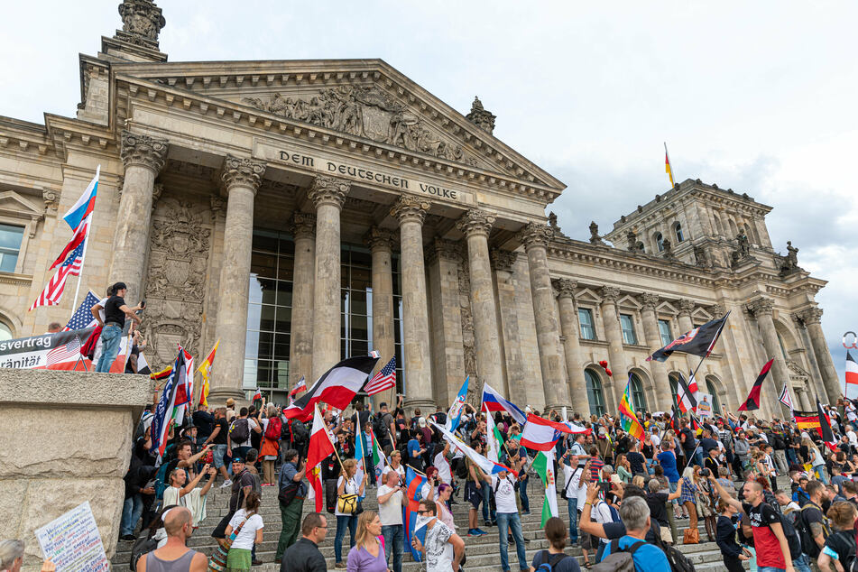 Teilnehmer einer Kundgebung gegen die Corona-Maßnahmen stehen auf den Stufen zum Reichstagsgebäude, zahlreiche Reichsflaggen sind zu sehen.