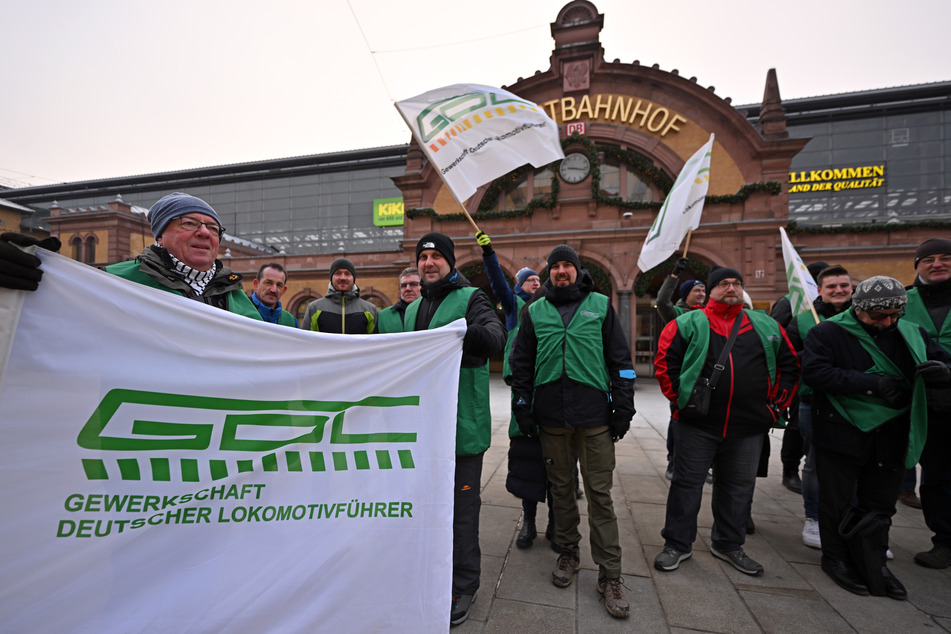 Mitglieder der Lokführergewerkschaft GDL stehen mit Fahnen vor dem Erfurter Hauptbahnhof.
