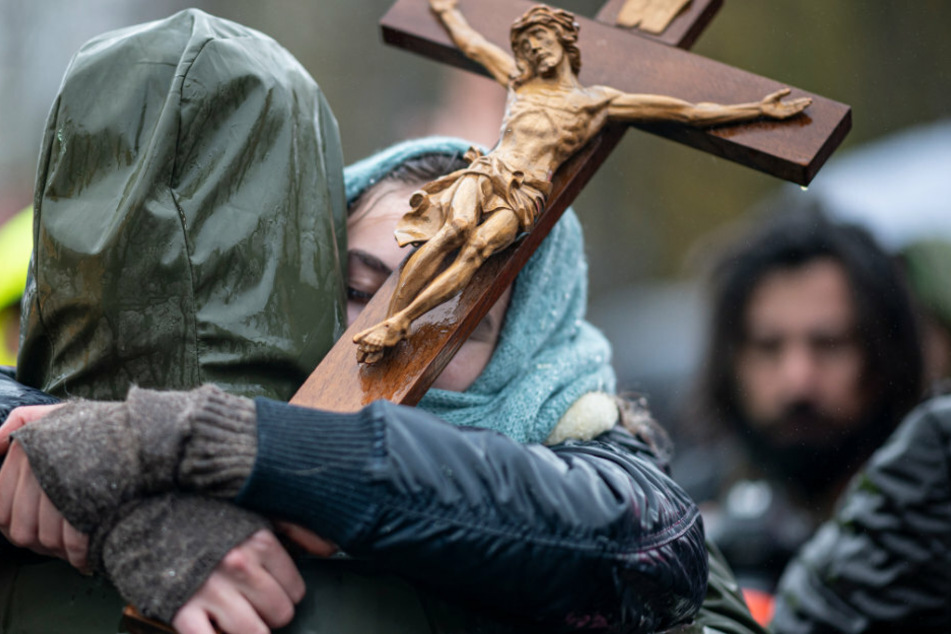 Zwei Teilnehmer der Demonstration gegen die Corona-Einschränkungen der Bundesregierung am Brandenburger Tor umarmen sich und halten ein Holzkreuz in der Hand.
