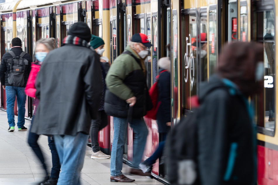 Fahrgäste mit Mund-Nasen-Bedeckungen steigen am Bahnhof Friedrichstraße in Mitte in eine S-Bahn ein.