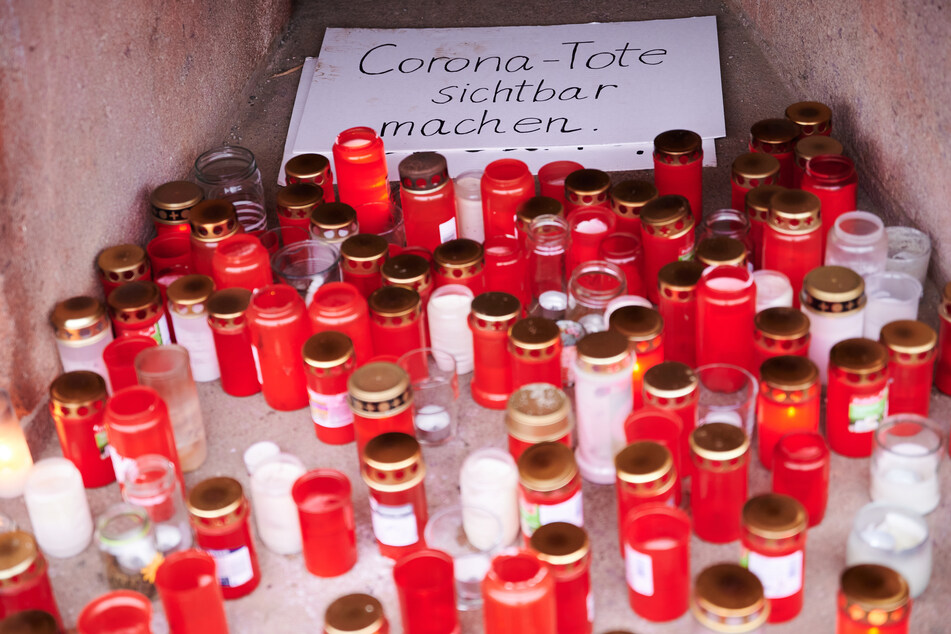 Mehrere Plakate, Grablichter und Kerzen stehen auf dem Podest des Stierbrunnens in Berlin, Prenzlauer Berg, und erinnern an die Toten durch Corona in Deutschland.