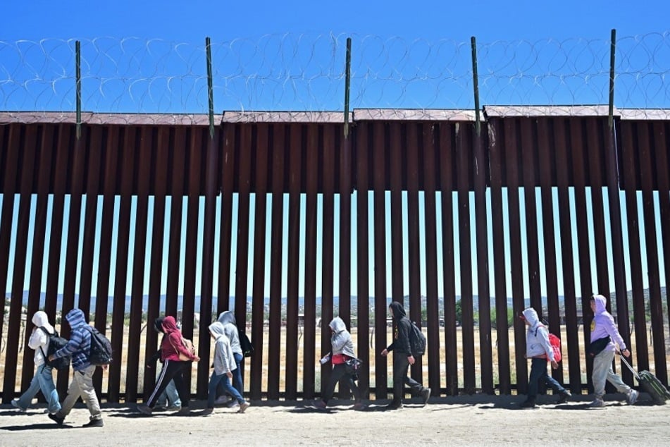 Migrants walk along the US side of the border wall in Jacumba Hot Springs, California, after crossing from Mexico.