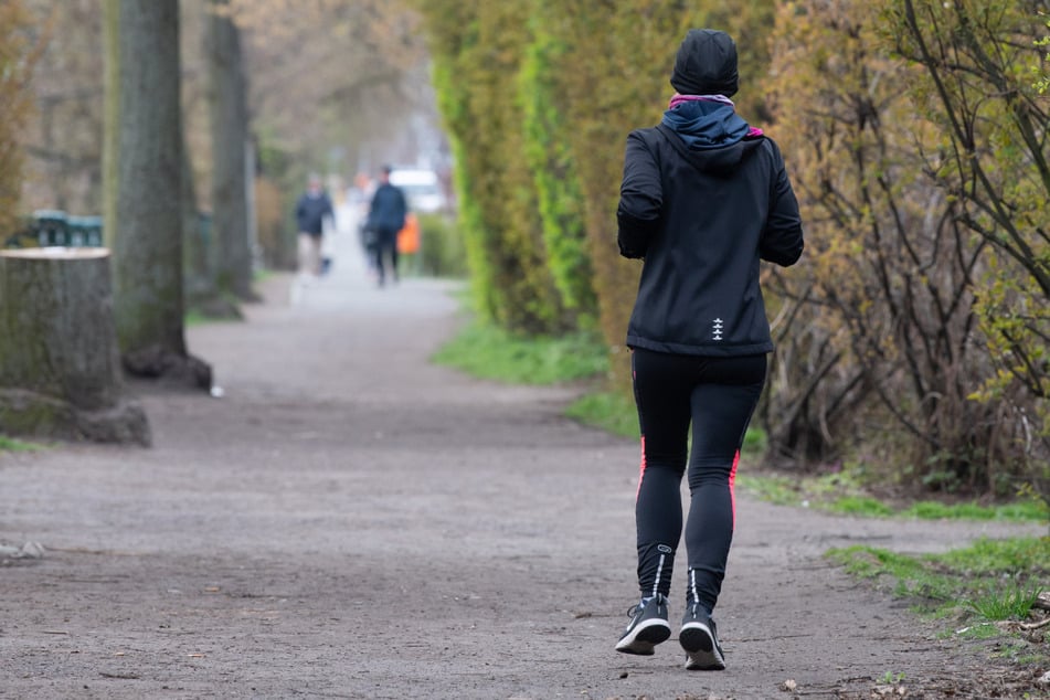 Eine Frau läuft dick eingepackt am Weigandufer in Neukölln entlang. Der Frühling in Berlin bleibt nass und frisch.