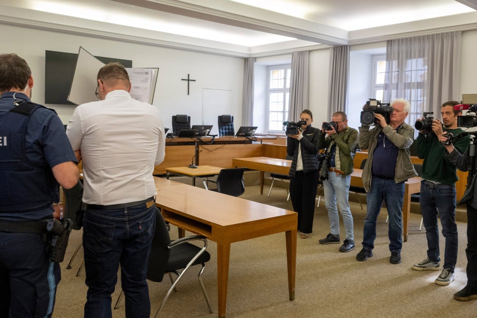 Der Beschuldigte versteckte sich hinter einem Aktenordner vor der Presse.