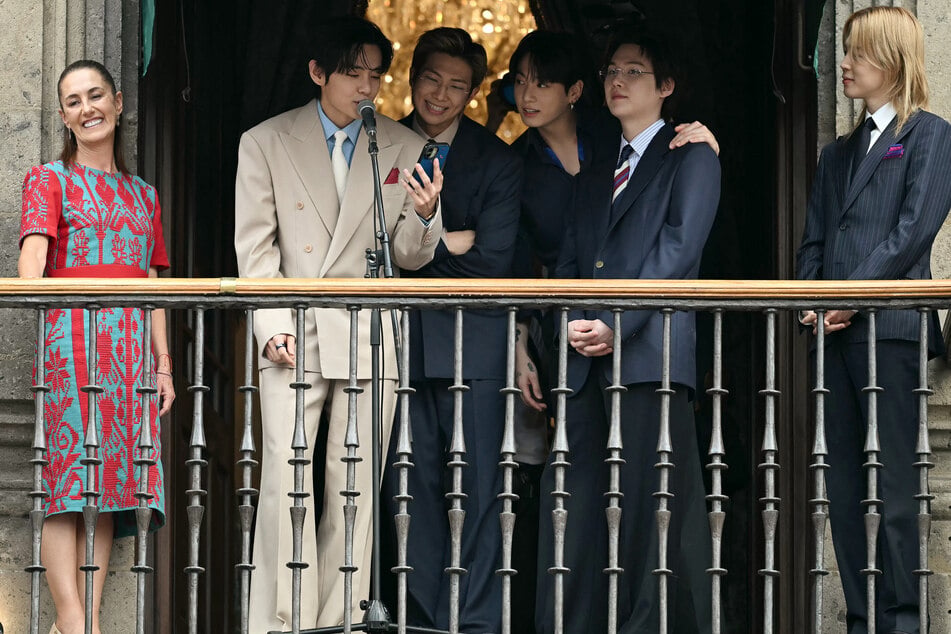Mexico's President Claudia Sheinbaum stands next to V, RM, Jung Kook, Suga, and Jimin from South Korean K-pop band BTS as they acknowledge fans from the balcony of the National Palace at Zocalo square in Mexico City on May 6, 2026.