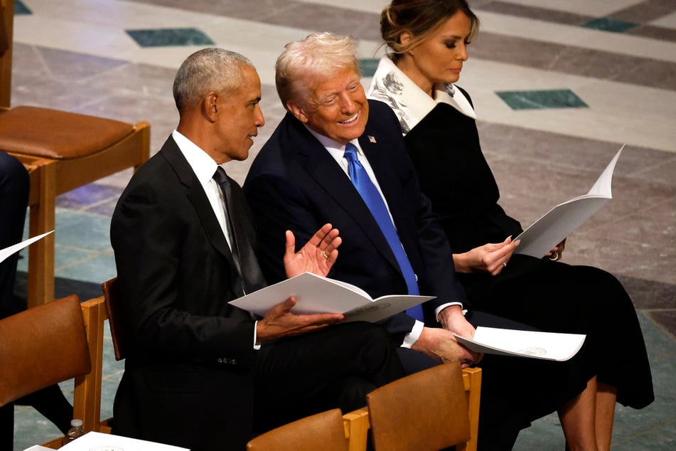 Former President Barack Obama speaks with Donald Trump as they sit side by side during the late President Jimmy Carter's funeral.