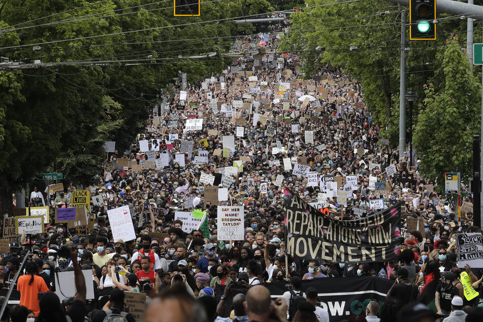Teilnehmer einer Kundgebung marschieren in Gedenken an den 19. Juni und zum Protest gegen die Polizeigewalt in den USA über die 23. Avenue und halten Schilder in die Höhe.