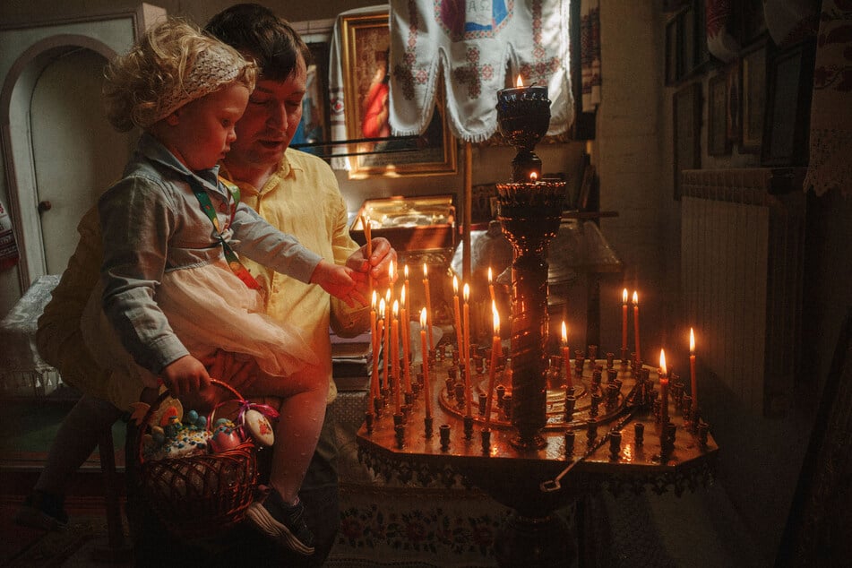 Ein Vater hilft seiner Tochter beim Anzünden einer Kerze während der orthodoxen Osterfeier in Charkiw.