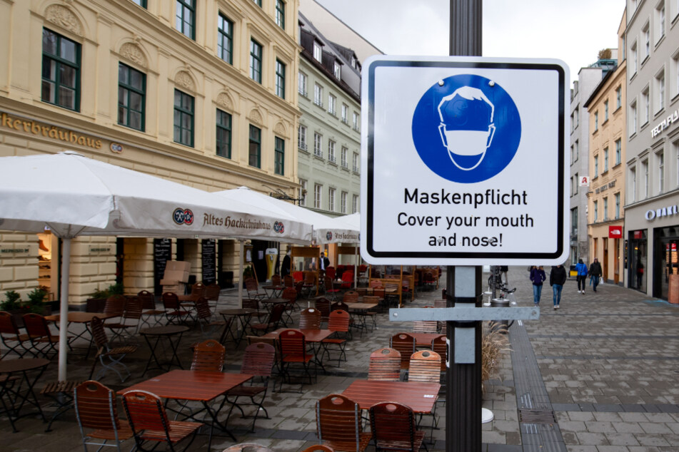 Ein Hinweisschild mit der Aufschrift "Maskenpflicht - Cover your mouth and nose!" steht in einer Fußgängerzone in der Münchner Innenstadt.