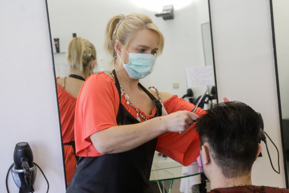 Eine Friseurin mit Mundschutz schneidet einem Kunden die Haare.