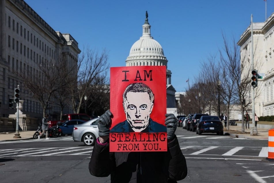 A person holds an "I Am Stealing From You" Elon Musk poster outside the US Capitol on in Washington DC.