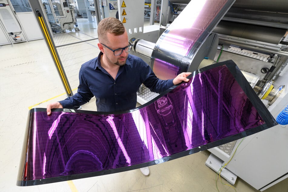 Heliatek-Sprecher Stephan Kube zeigt in einer Produktionshalle die biegsame organische Solarfolie.
