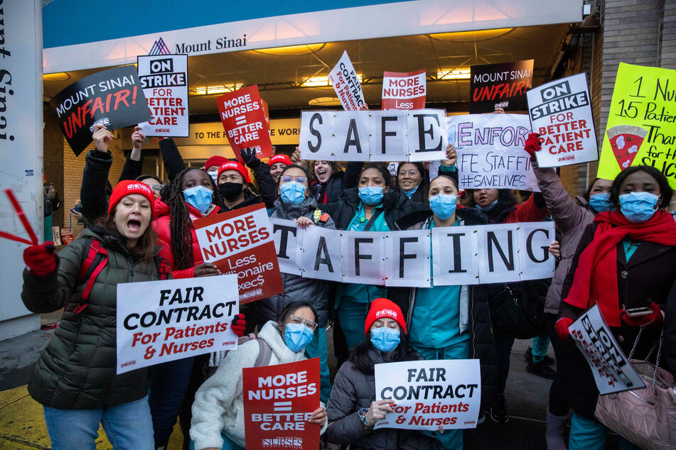 New York City nurses on strike raise signs demanding safe staffing ratios.
