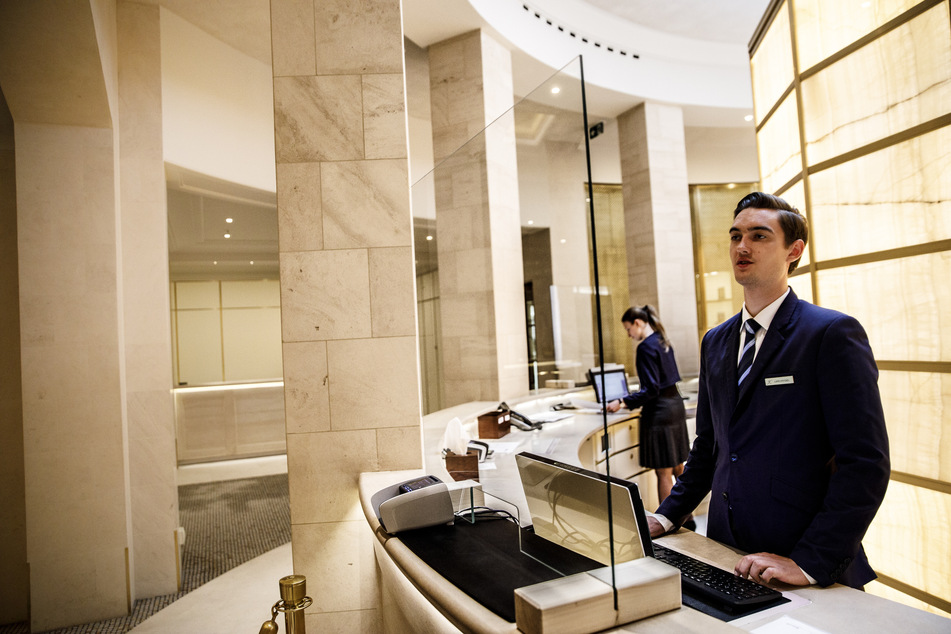 Ein Mitarbeiter steht hinter einer Schutzscheibe an der Rezeption in der Lobby im Hotel Adlon Kempinski am Pariser Platz in Berlin.