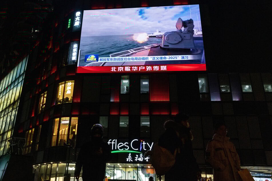 People walk by a giant screen during a broadcast of news on China's military drills around Taiwan, in Beijing on December 29, 2025.