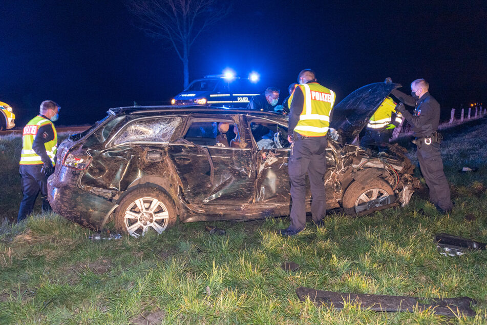Einsatzkräfte stehen neben dem völlig zerstörten Fahrzeug.