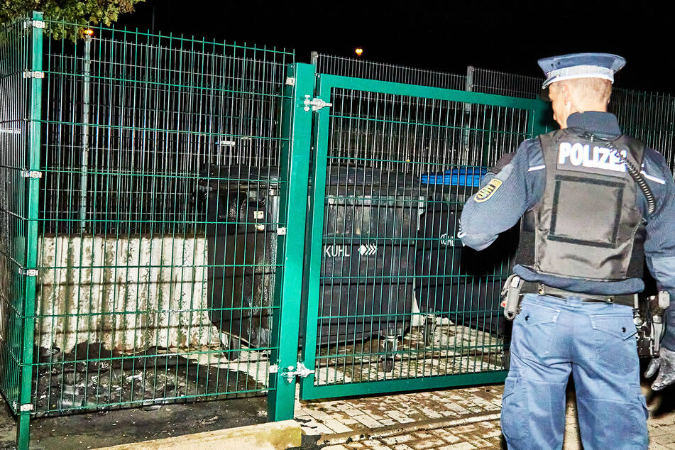Ein Beamter nimmt die Überreste einer abgebrannten Mülltonne in Augenschein.