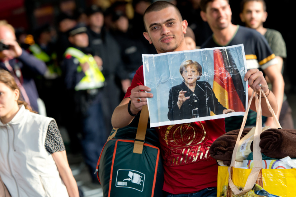 Ein Flüchtling, der kurz zuvor mit einem Zug angekommen ist, läuft auf dem Hauptbahnhof München über den Bahnsteig und hält dabei ein Foto von Angela Merkel in den Händen. (Archiv)