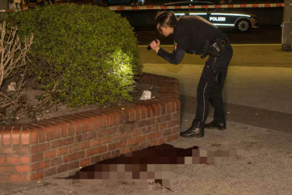Eine Polizistin sucht mit einer Taschenlampe ein Gebüsch nach Spuren ab.