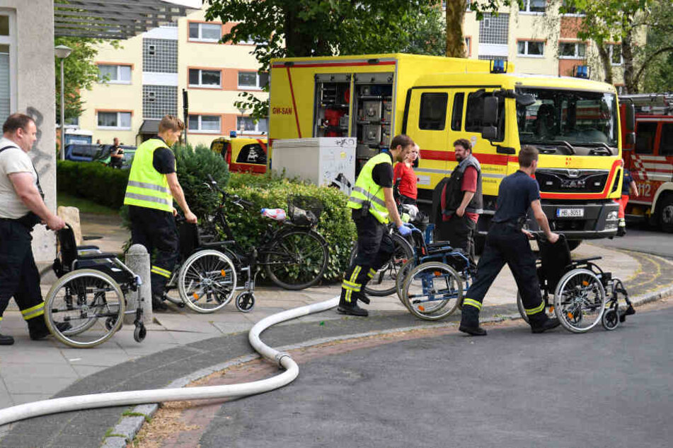 Einsatzkräfte schieben leere Rollstühle aus einem Pflege- und Altenheim. Das gesamte Dach des Heims ist abgebrannt. 96 Menschen mussten nach Informationen der Feuerwehr aus dem Gebäude gerettet werden.
