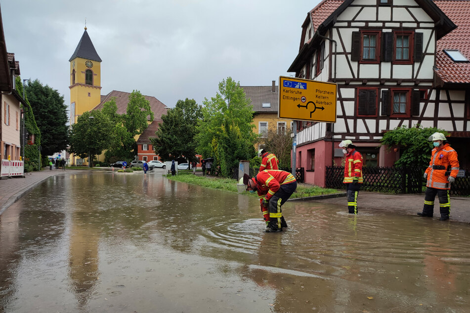 Karlsbad am Sonntag: Feuerwehrleute stehen nach einem Unwetter auf einer überfluteten Straße.