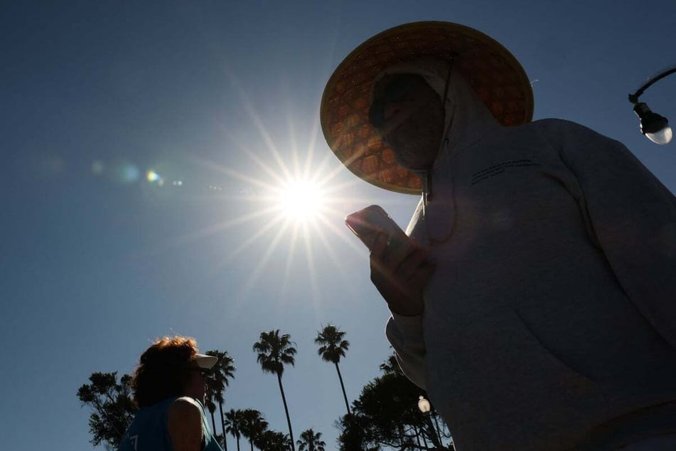 A person wears a hat for shade under the morning sun while walking along The Strand in Redondo Beach, California on March 20, 2026, during a heat wave.