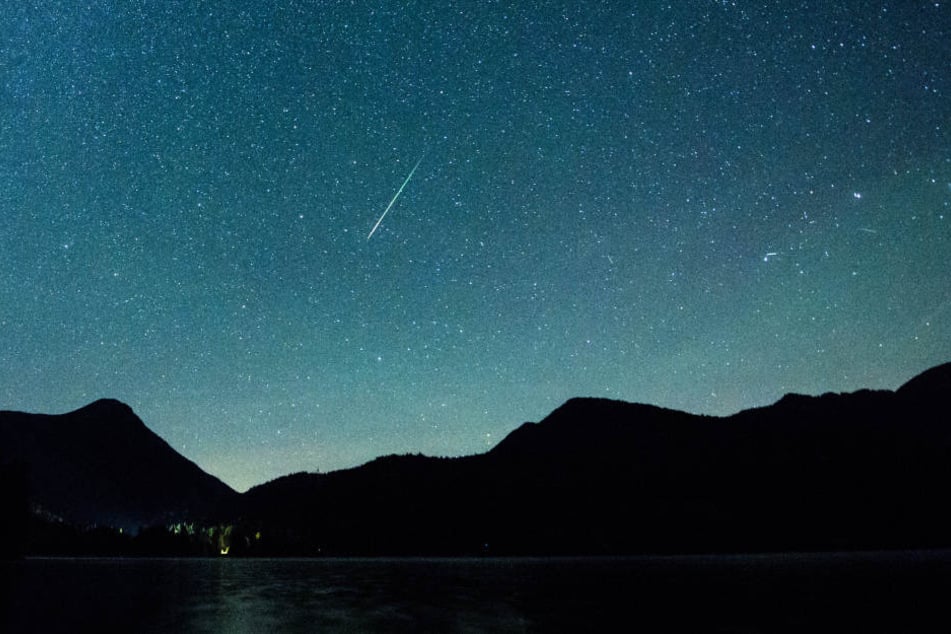 Eine Sternschnuppe leuchtet neben der Milchstraße am Himmel.