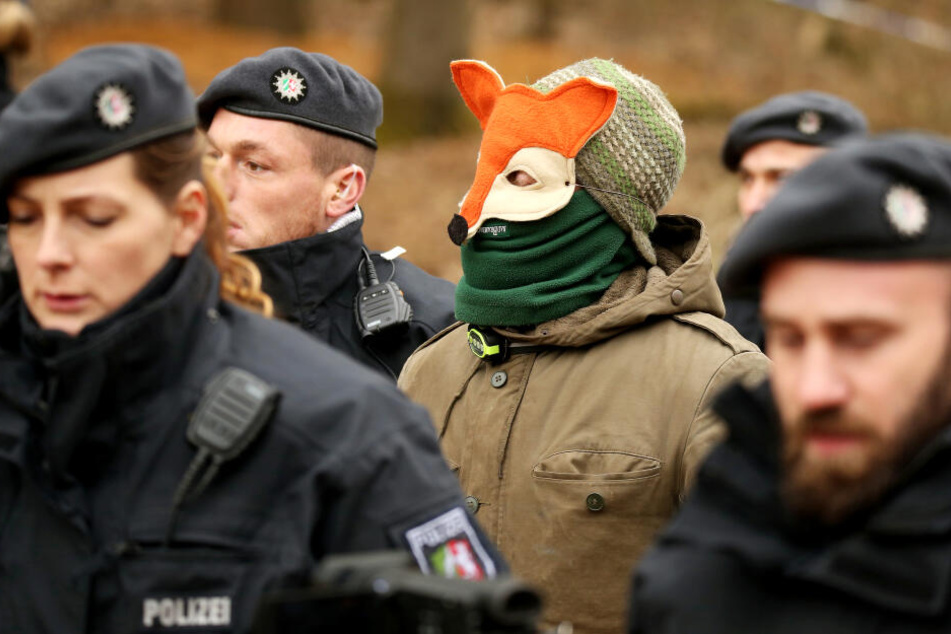 Ein Vermummter geht mit Polizisten zur Überprüfung der Personalien zu einem Einsatzfahrzeug.