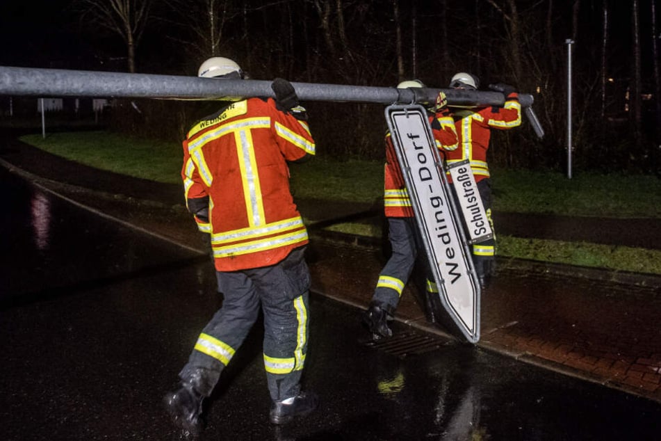 Feuerwehrleute tragen ein vom Wind umgewehtes Straßenschild weg.