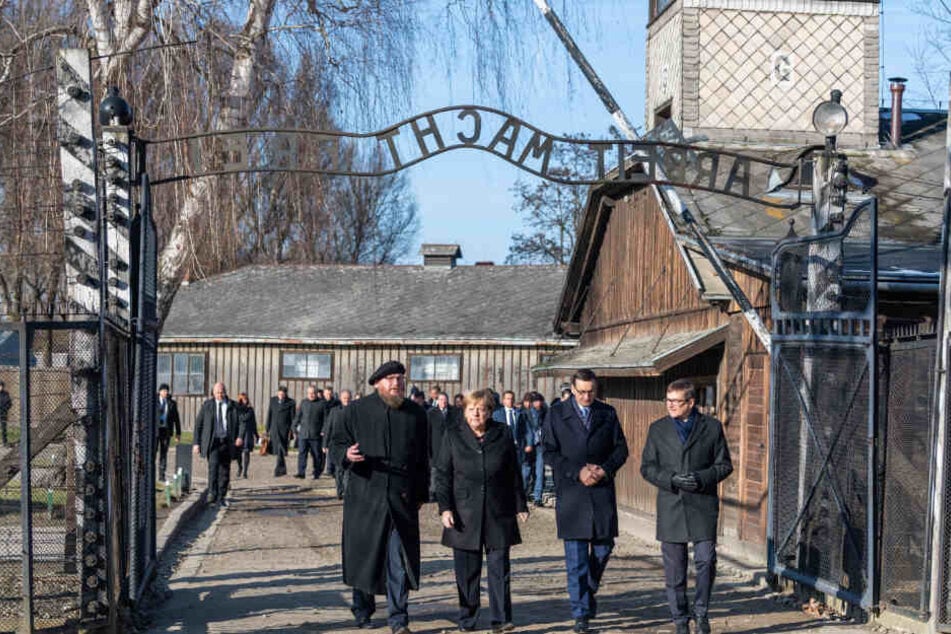 Angela Merkel steht mit Mateusz Morawieckiund dem Direktor der Gedenkstätte, Piotr Cywinski unter dem Eingangstor mit dem Schriftzug "Arbeit macht frei".