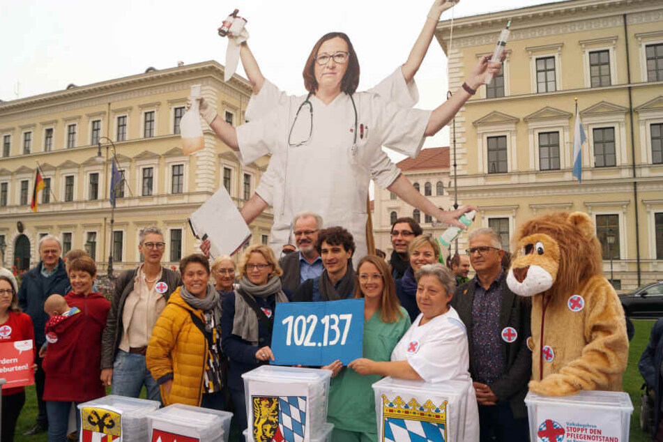 Natascha Kohnen, SPD-Landesvorsitzende, Ates Gürpinar, Landesvorsitzender der bayerischen Linken, und Pflegekräfte halten ein Schild mit der Zahl 102.137. Mehr als 100.000 Menschen in Bayern haben sich mit ihrer Unterschrift für ein Volksbegehren gegen de