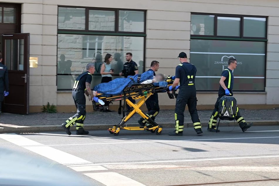 Noch mit dem Messer im Rücken wird der Zahnarzt auf einer Fahrtrage zum Rettungswagen gebracht.
