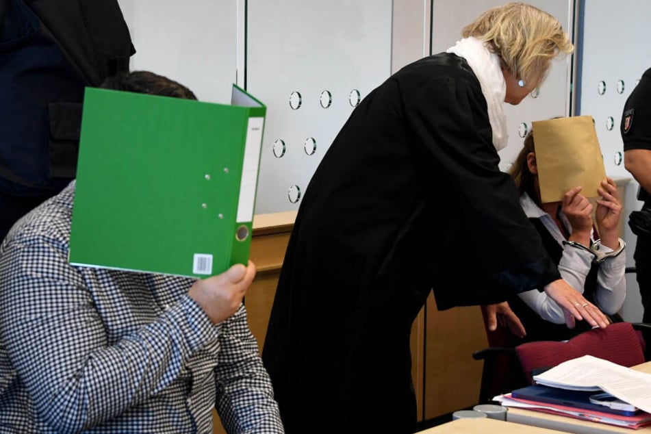 Mit verdeckten Gesichtern sitzen die Angeklagten zum Auftakt eines Mordprozesses im Gerichtssaal.