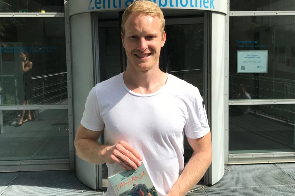Der Sportstudent Tim Jost (25) mit seinem Buch vor der Kölner Sporthochschule.