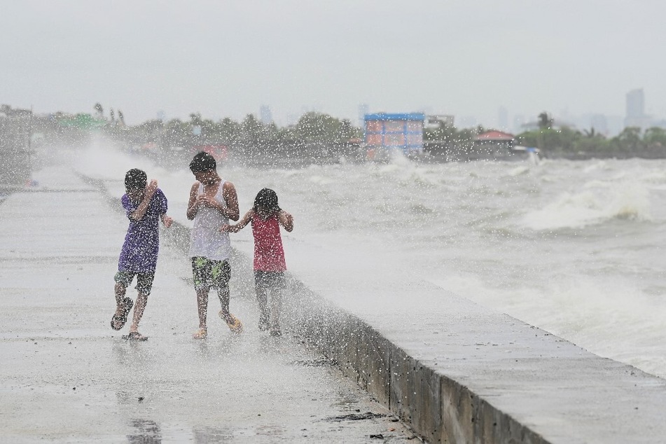 Children walk along a sea wall at Navotas in Metro Manila on July 26, 2023, as Super Typhoon Doksuri passes close to the northern tip of Luzon island.