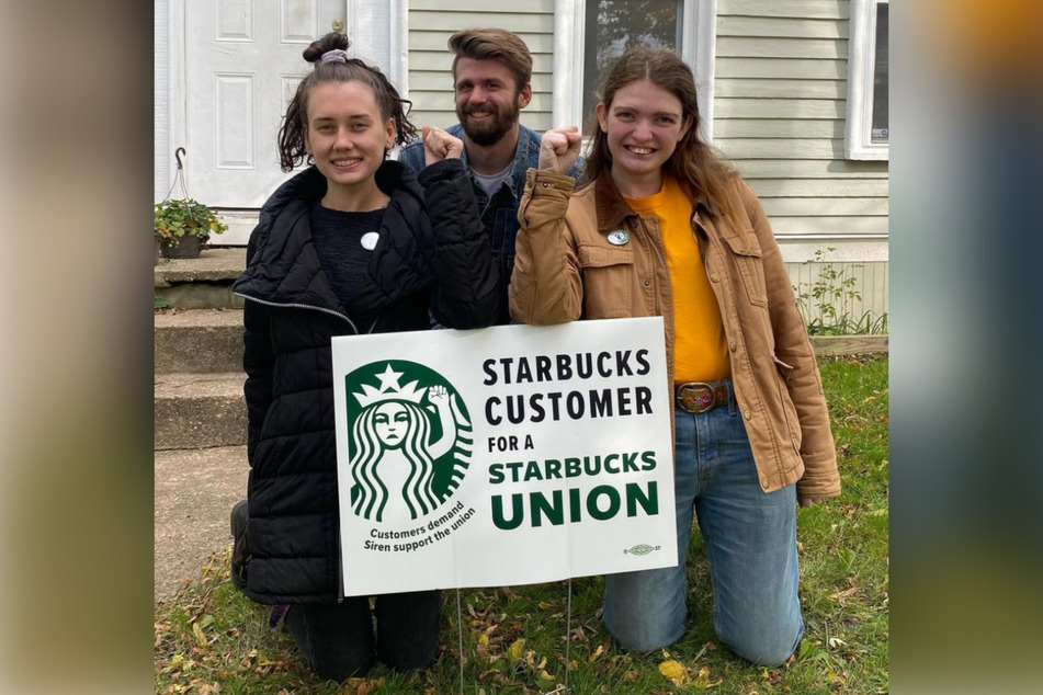 Jaz Brisack (r.) and her partners pose in front of a Starbucks Workers United yard sign in Buffalo.