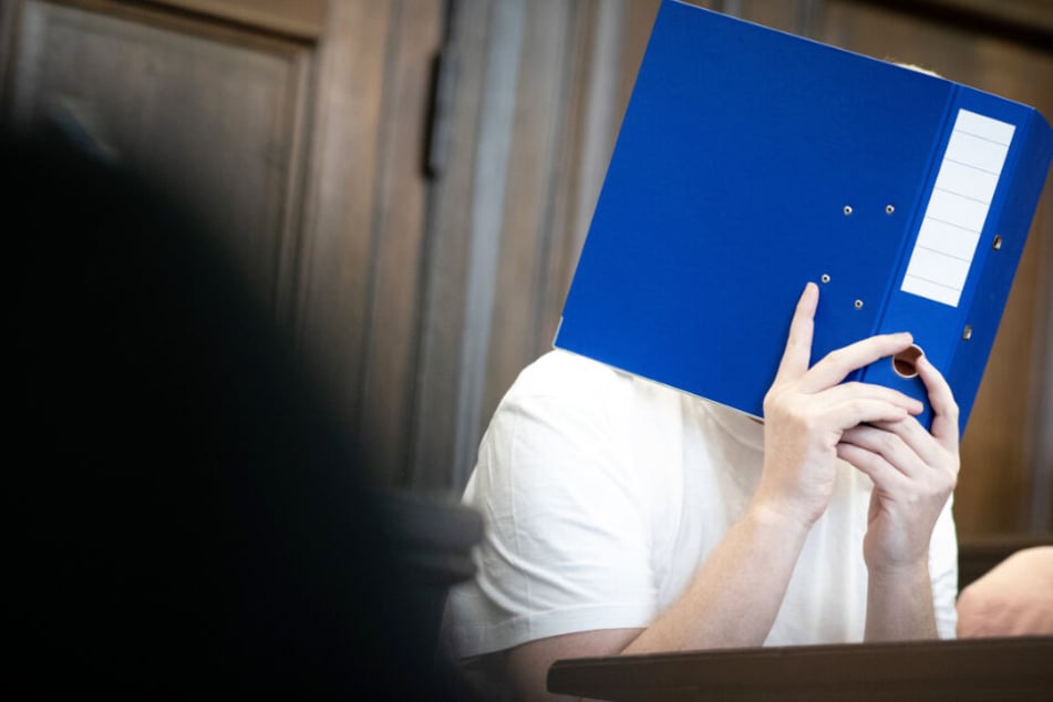 Der Angeklagte verbirgt sein Gesicht kurz vor Prozessbeginn hinter einem Aktenordner.