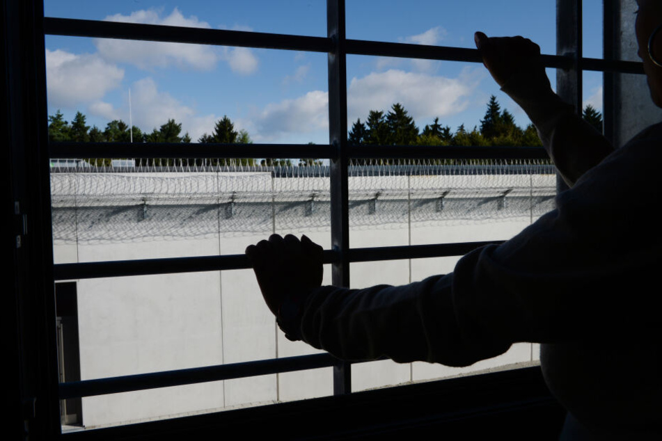 Ein Häftling steht in einer Justizvollzugsanstalt an einem vergitterten Fenster in einer Zelle.