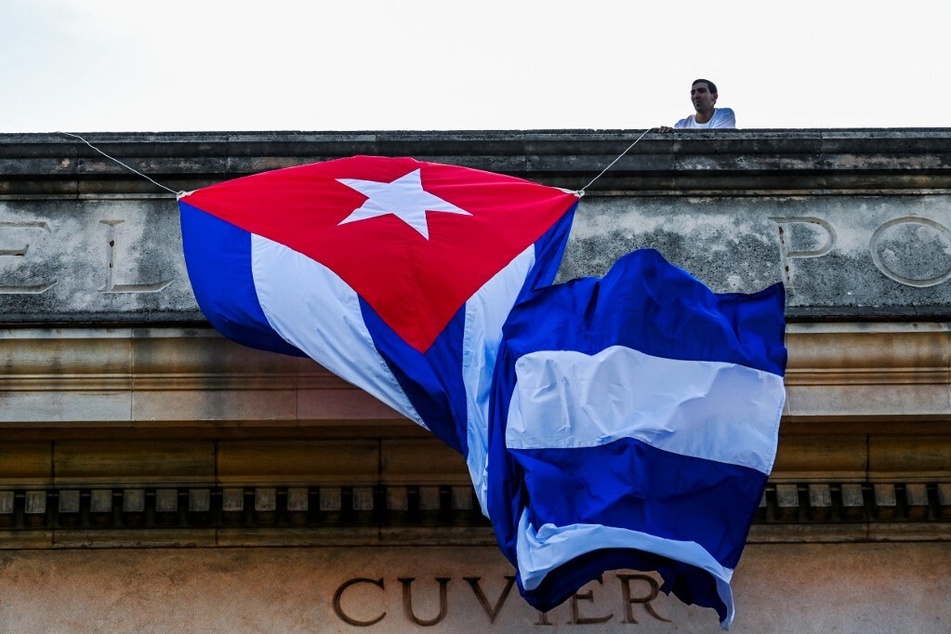 A man unfurls a Cuban flag from the roof of the University of Havana.