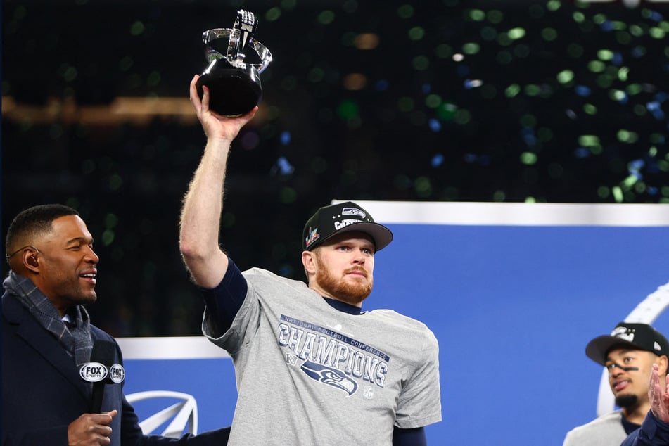 Seattle Seahawks quarterback Sam Darnold celebrates with the trophy on the podium after defeating the Los Angeles Rams in the 2026 NFC Championship Game at Lumen Field.