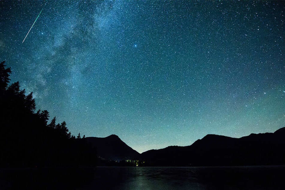 Eine Sternschnuppe leuchtet neben der Milchstraße am Himmel über dem Walchensee.