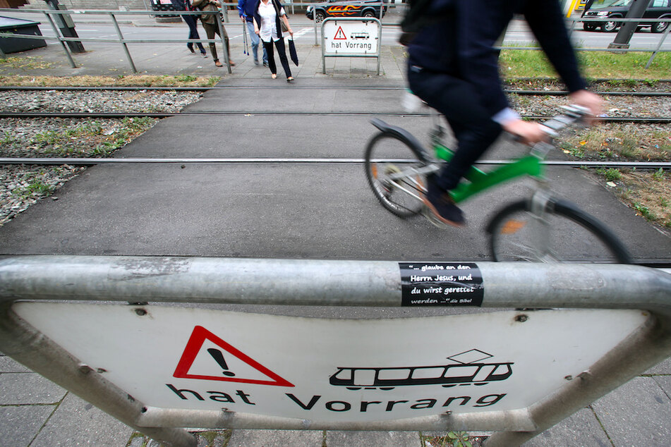 Radfahrer und Fußgänger queren Straßenbahnschienen in München.