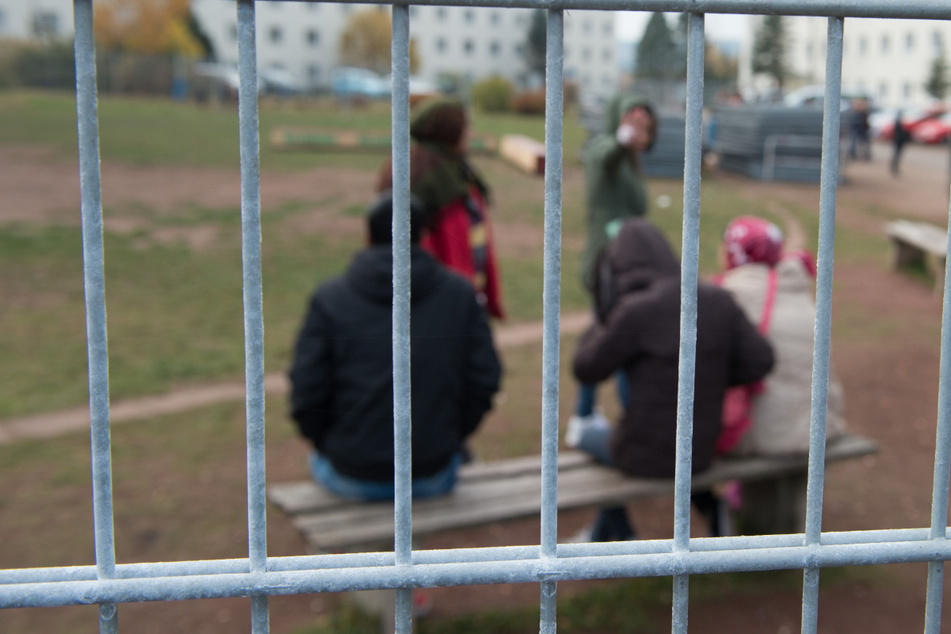 Flüchtlinge sitzen hinter einem Zaun auf dem Gelände der Erstaufnahmestelle. (Symbolbild)