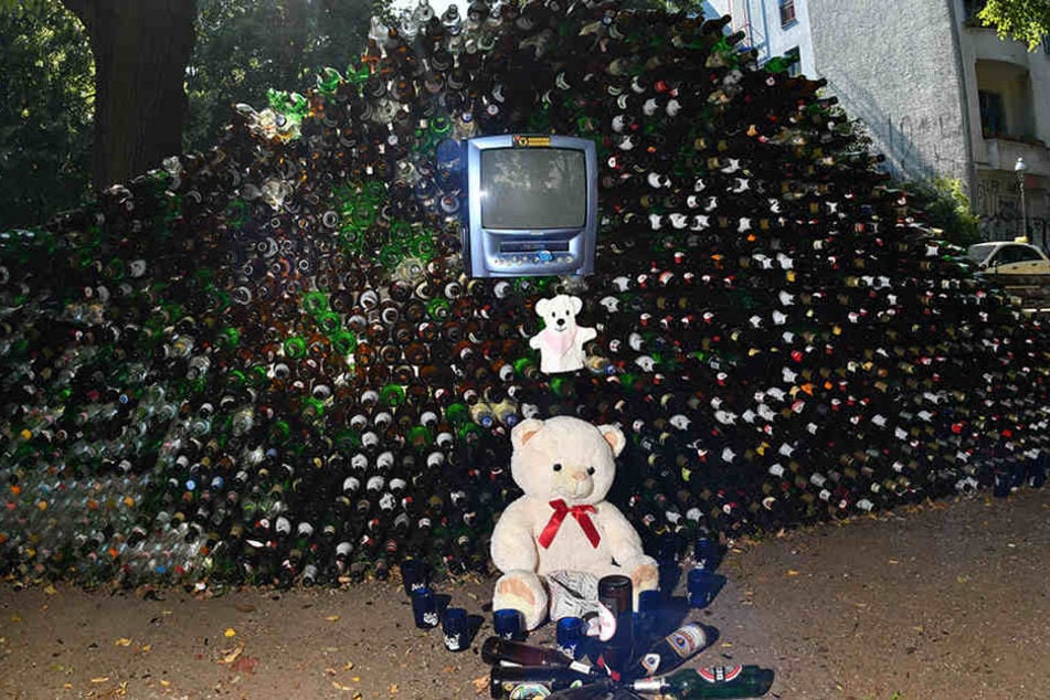Ein Teddy-Bär ziert die Front der Wand aus Glasflaschen.