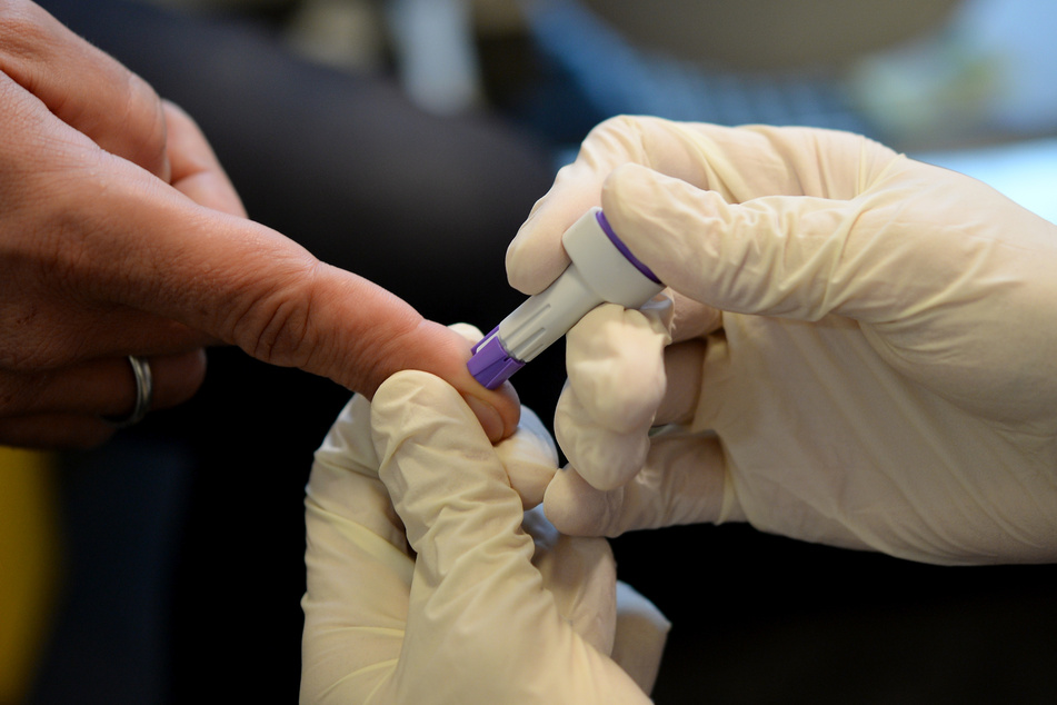 Ein Arzt nimmt in einer Einrichtung des Aids-Hilfe e.v. an dem Finger eines jungen Mannes Blut ab.