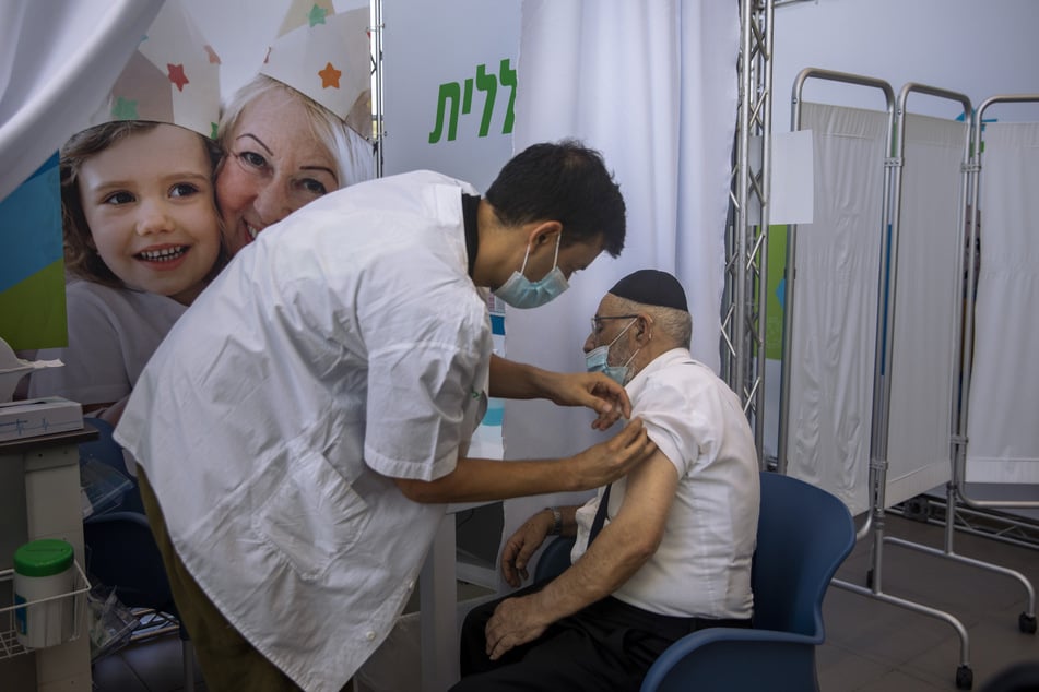 Israel, Tel Aviv: Ein Mann erhält eine dritte Dosis des Corona-Impfstoffes von Biontech/Pfizer von einem medizinischen Mitarbeiter in einem Impfzentrum.